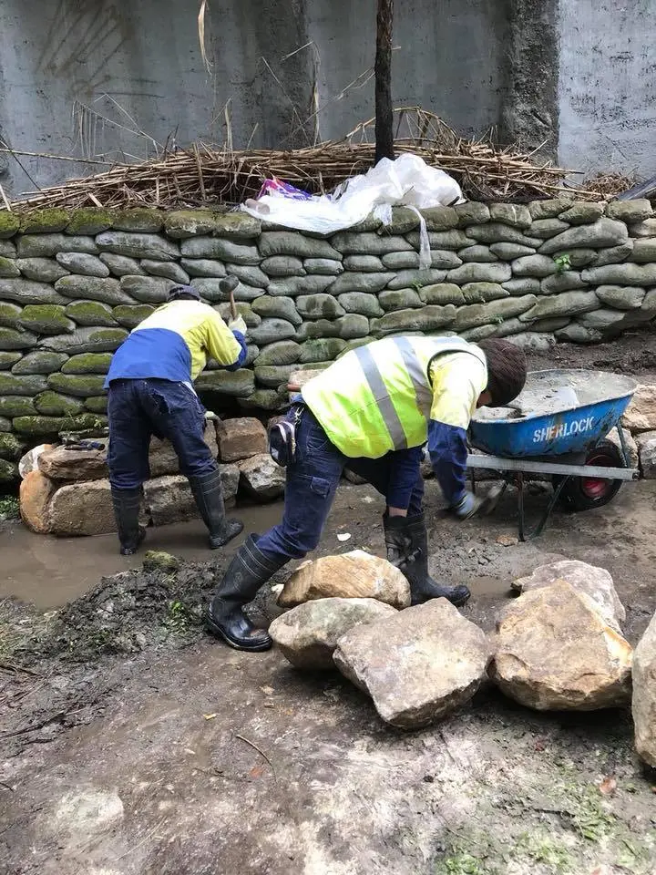 Stonemasons constructing natural rock erosion protection beside an existing wall